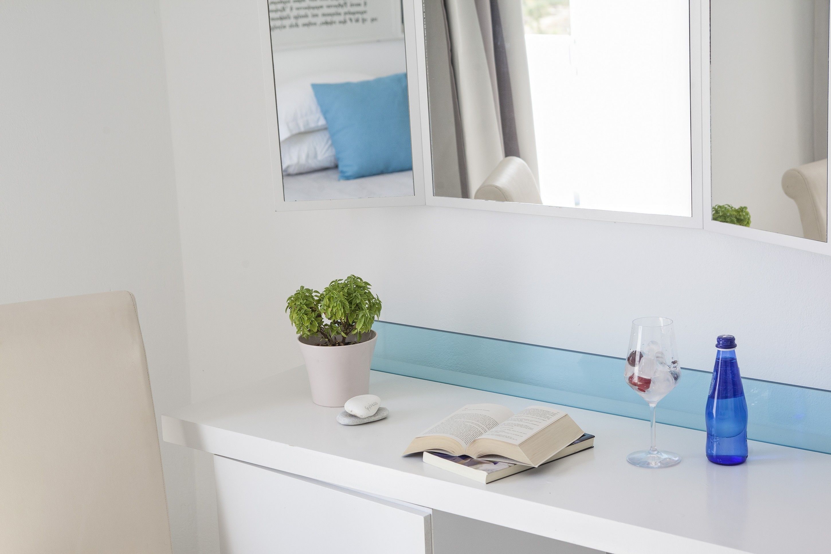 Een schoon, modern bureau met een potplant, een boek, een glas water en een blauwe fles.