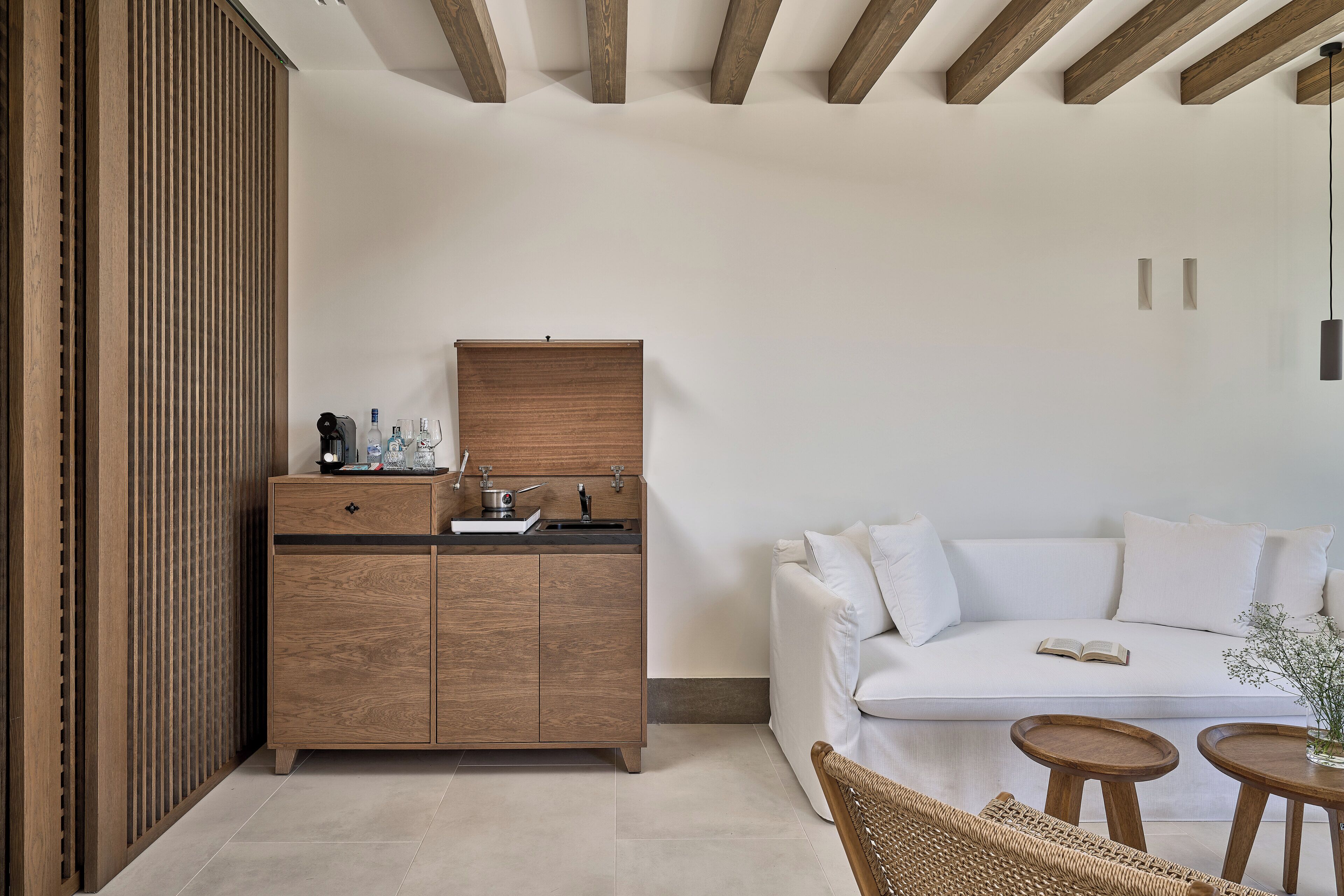 A modern, minimalist room with a wooden cabinet, a white sofa, and a wicker chair.