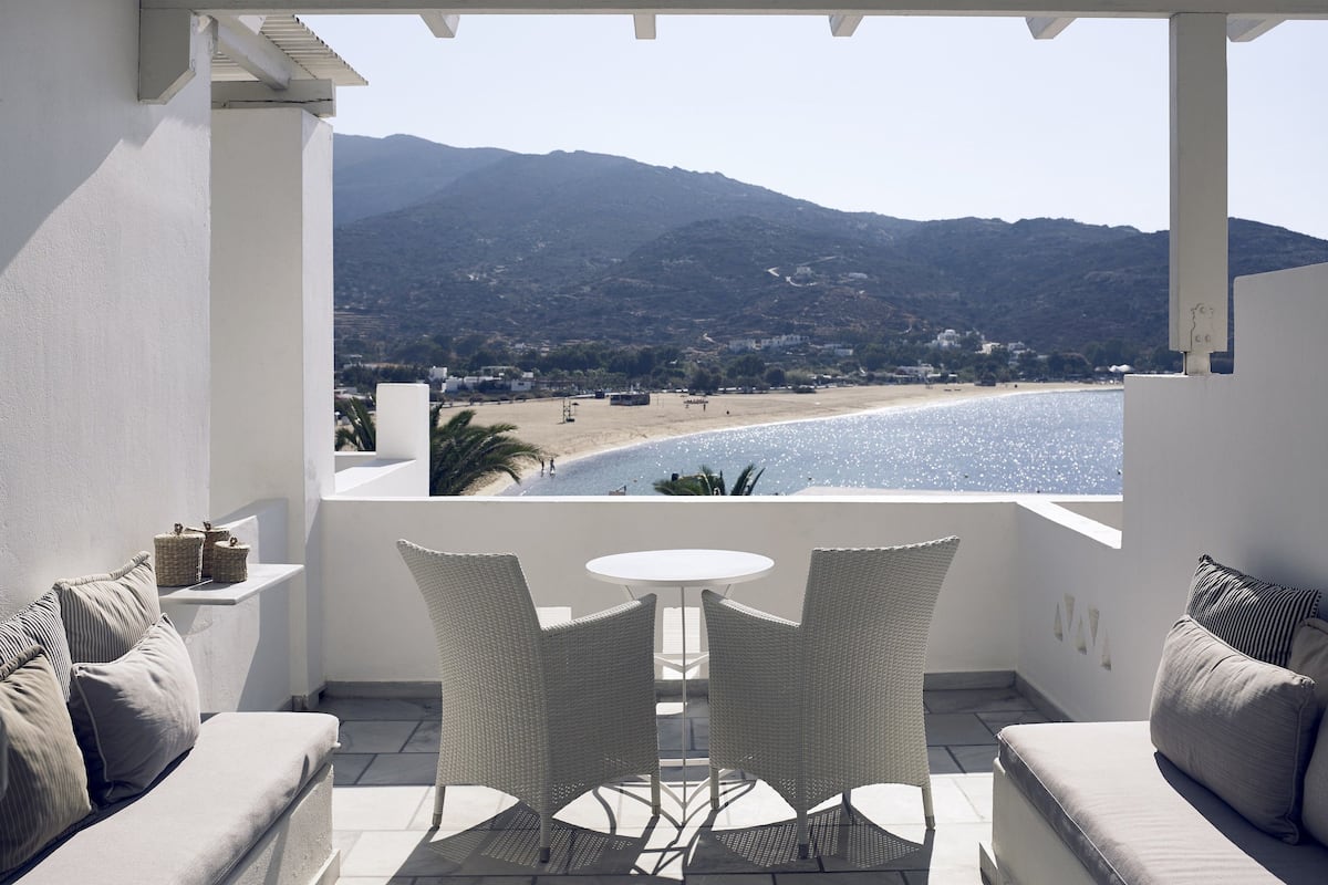 A balcony with wicker furniture, a view of a beach, and mountains in the distance.