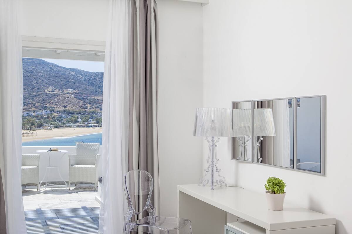 A modern hotel room with a balcony overlooking a beach and mountains.