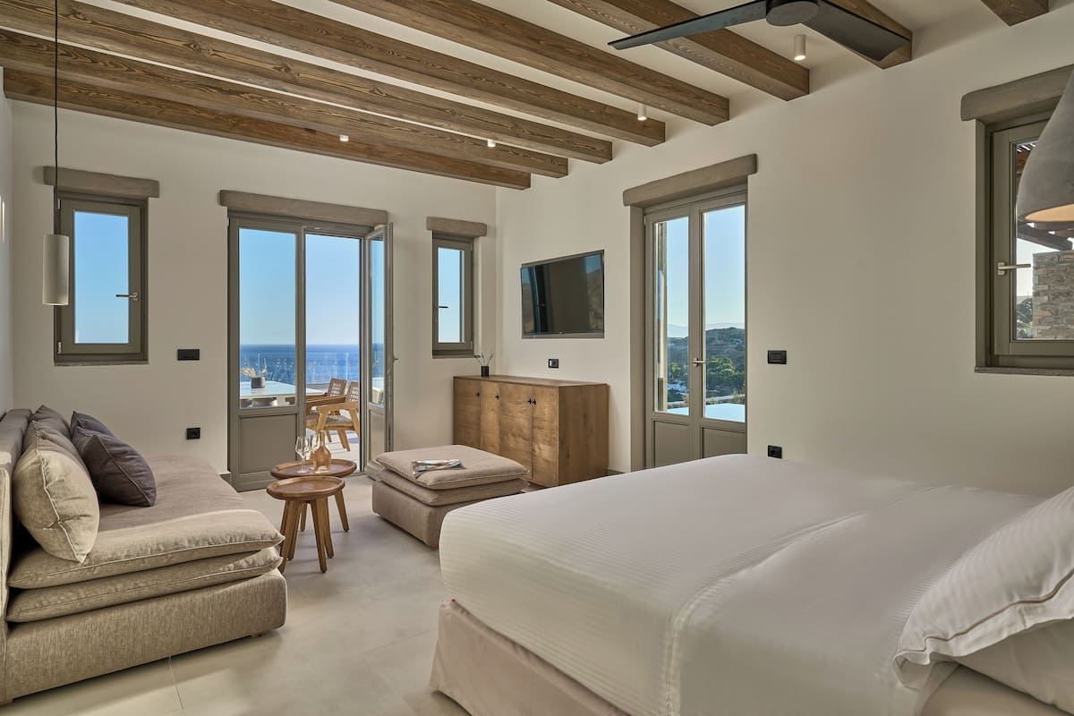 A modern bedroom with a large bed, a sofa, a wooden cabinet, and a TV on the wall.