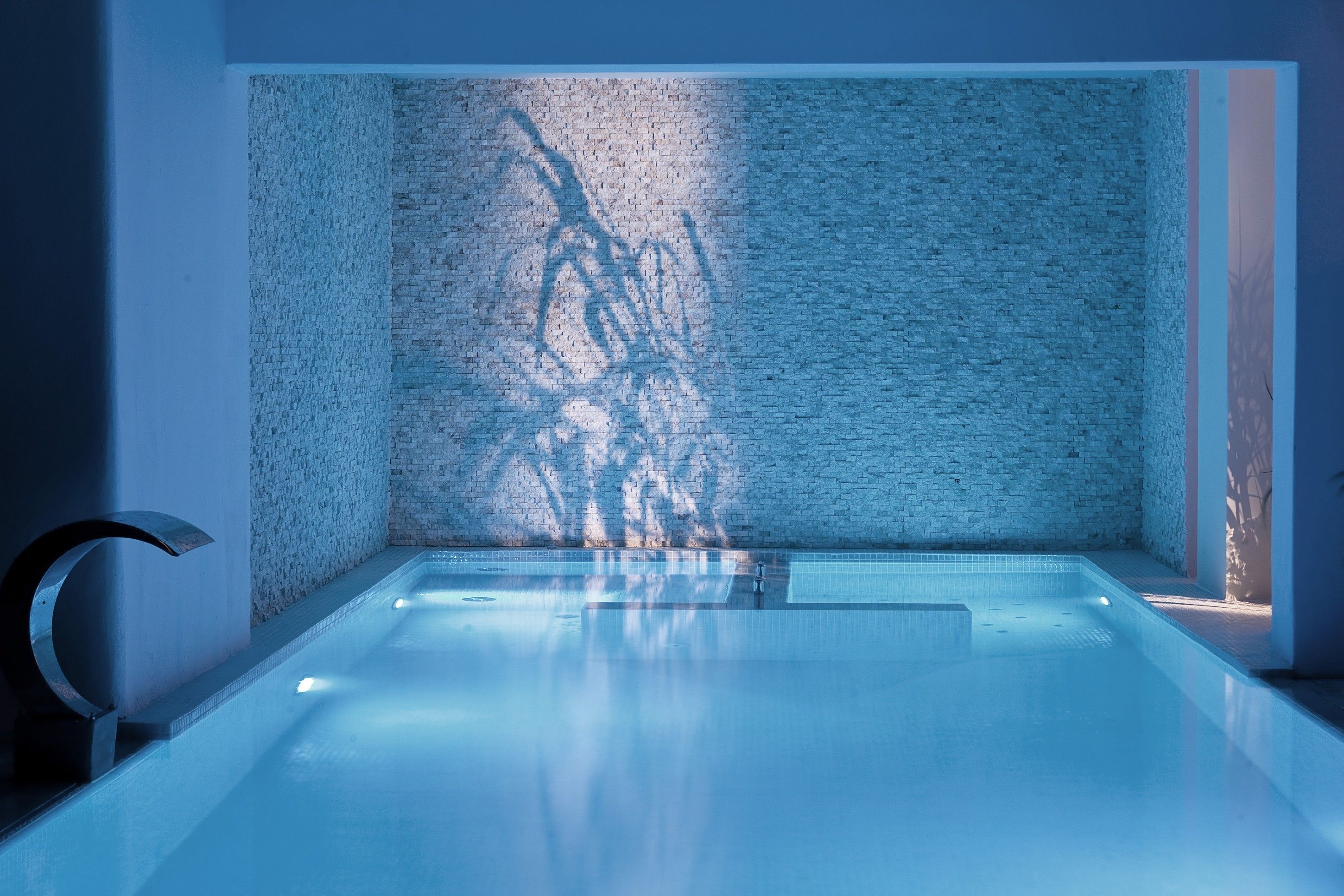 Una piscina interior moderna con pared texturizada y superficie de agua cristalina.