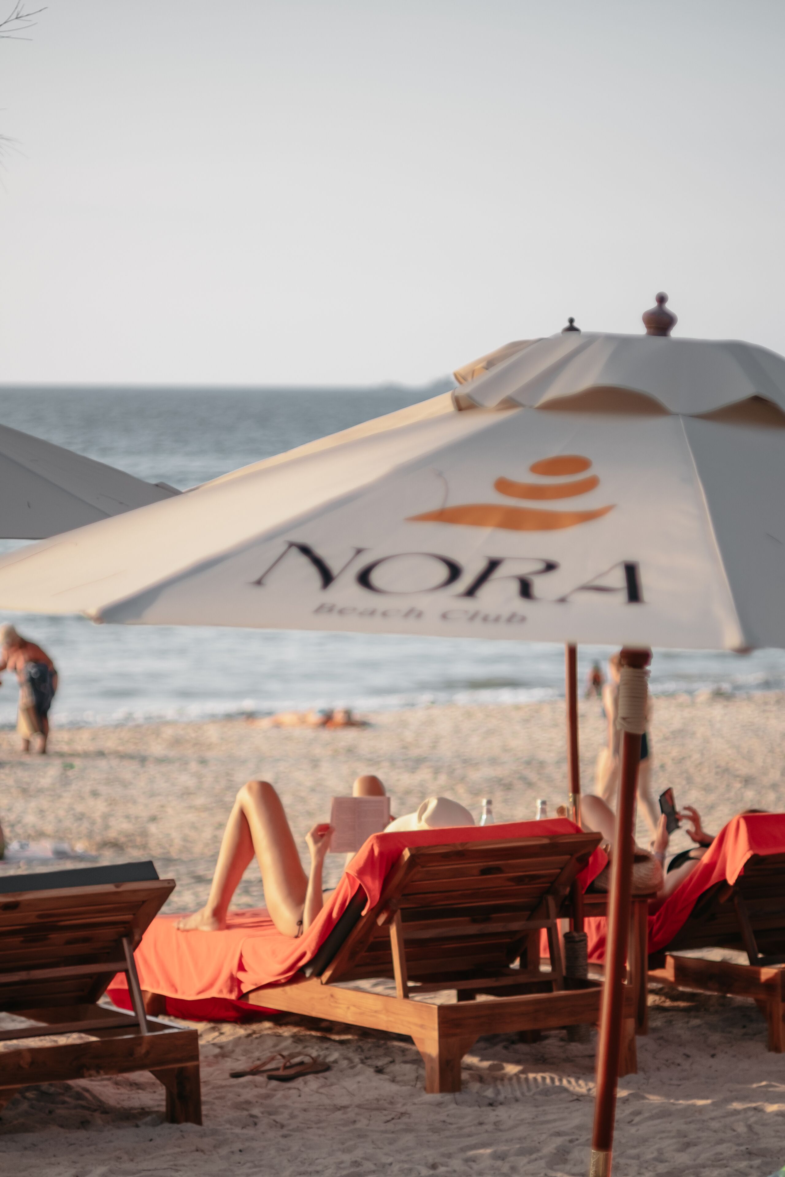A beach setting with lounge chairs and a beach umbrella labeled "NORA Beach Club".