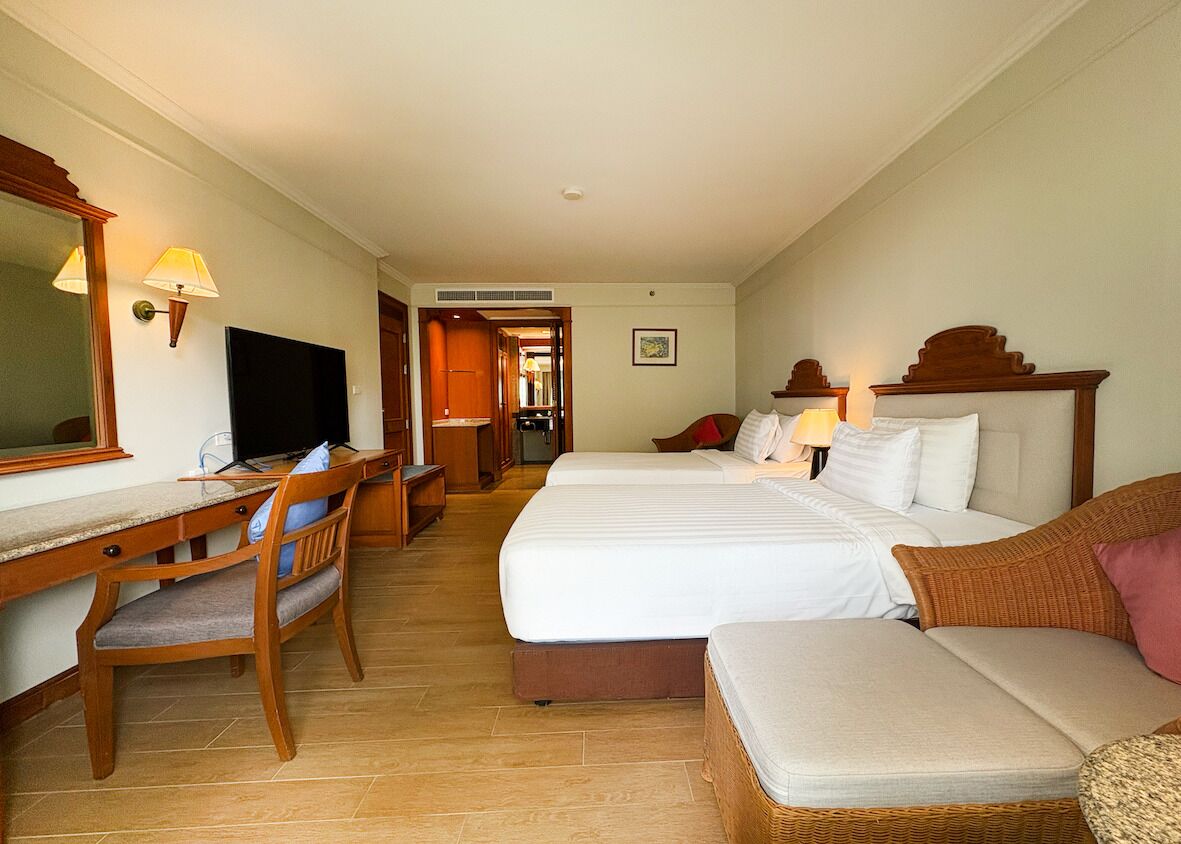 Ein Hotelzimmer mit zwei Betten, einem Schreibtisch, einem Computer, einem Stuhl und einem Fernseher.