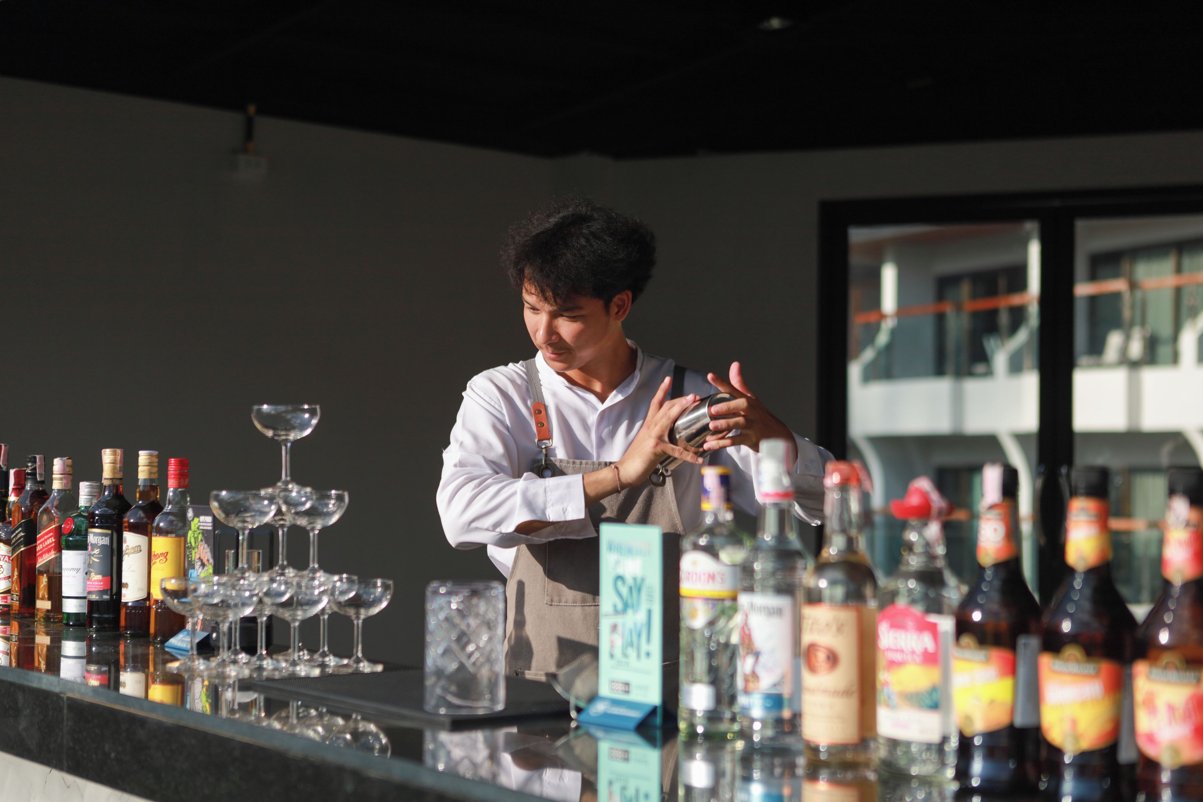A bartender preparing a drink at a bar with various bottles and glasses.
