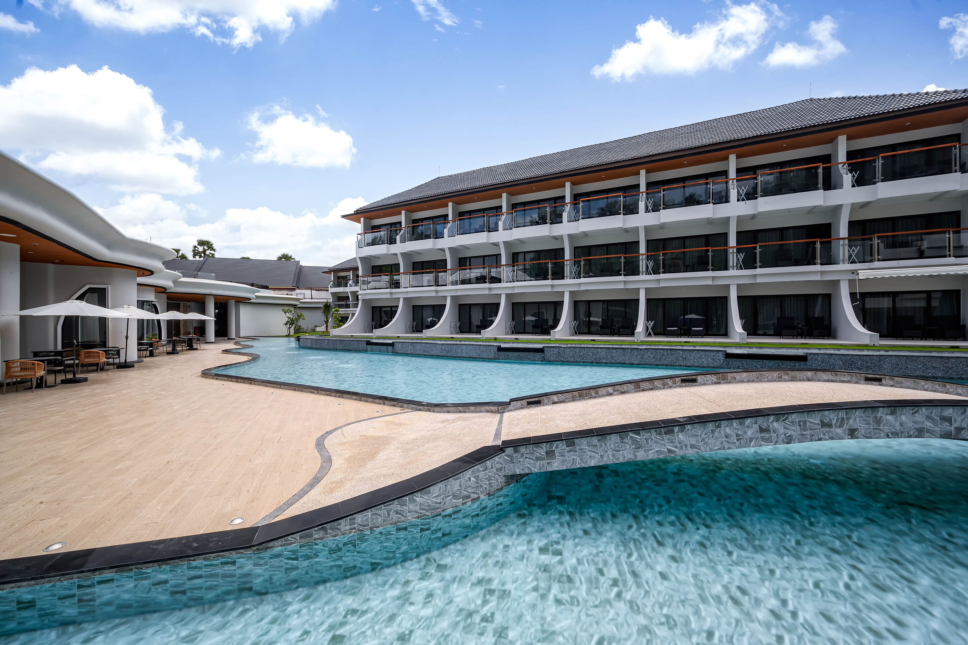 A modern hotel with a large pool, outdoor seating, and multiple balconies.
