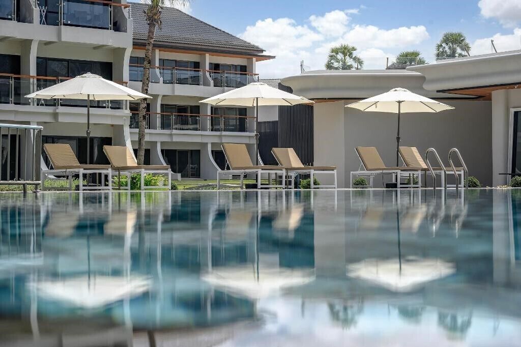 Un hotel moderno con área de piscina, sillones de descanso y sombrillas.