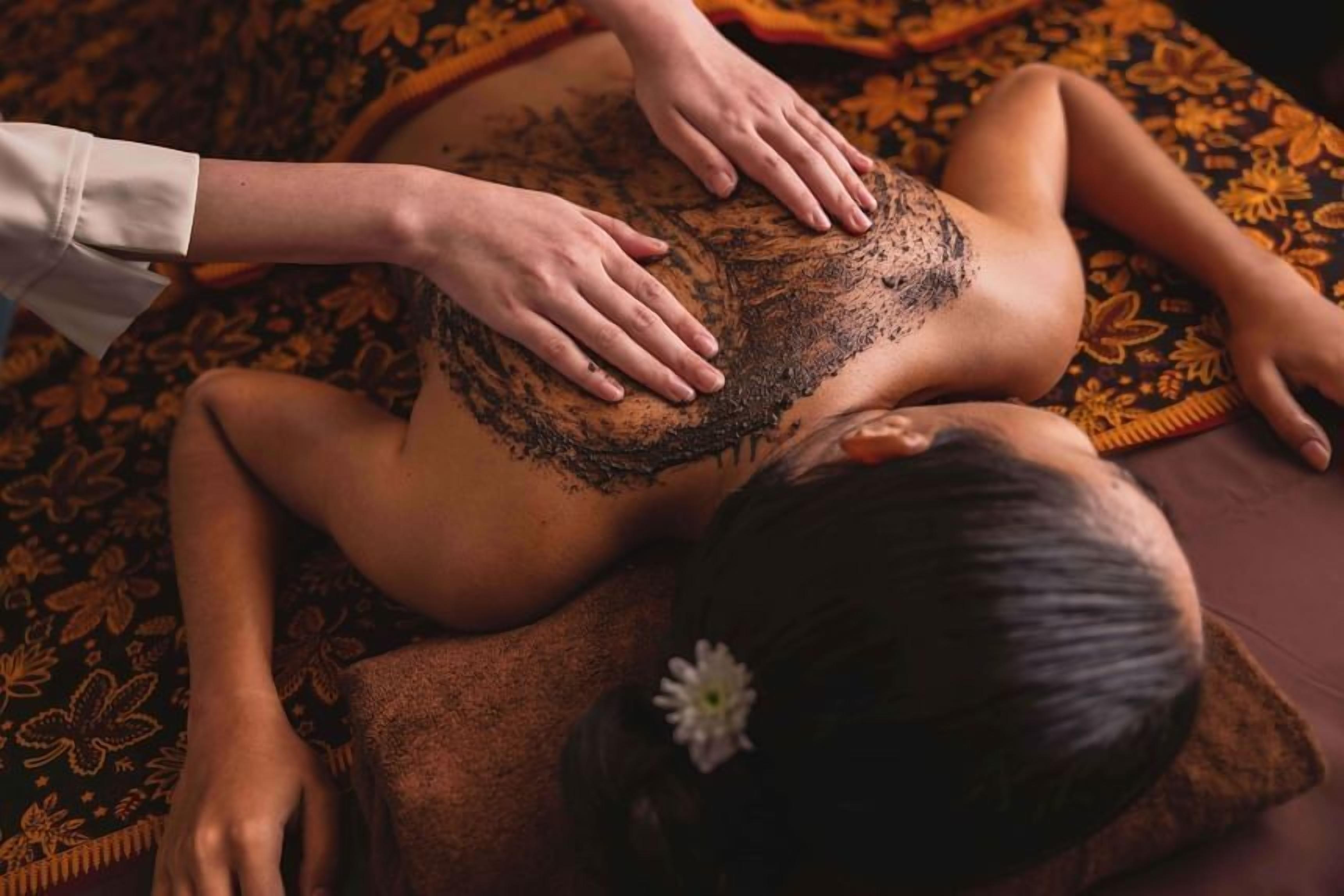 En person modtager massage med hænder på ryggen, liggende på en mønstret måtte.