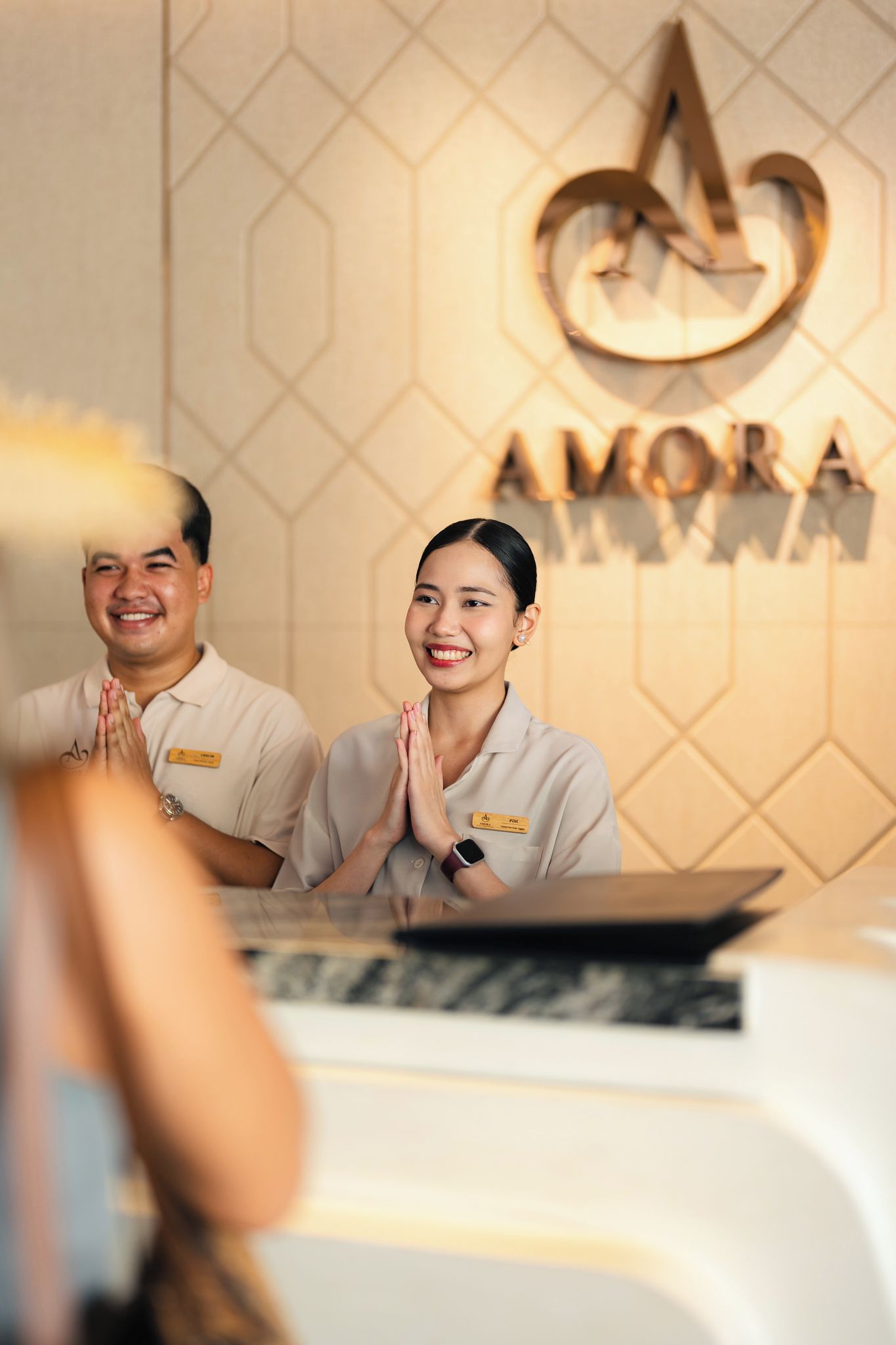 Two individuals seated at a reception desk with a logo above them.