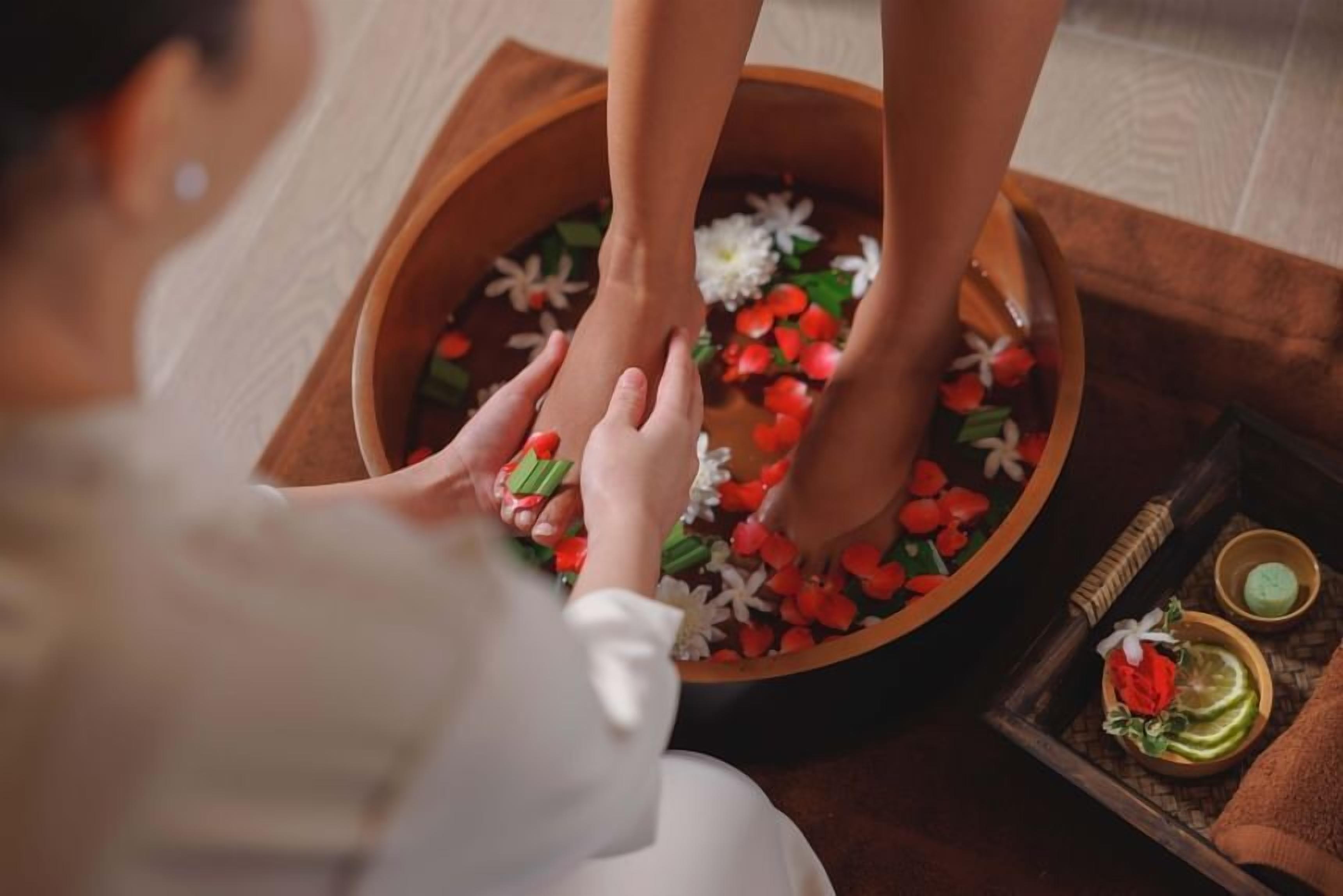 A foot soak with flowers and a small tray with a candle and a green bottle.