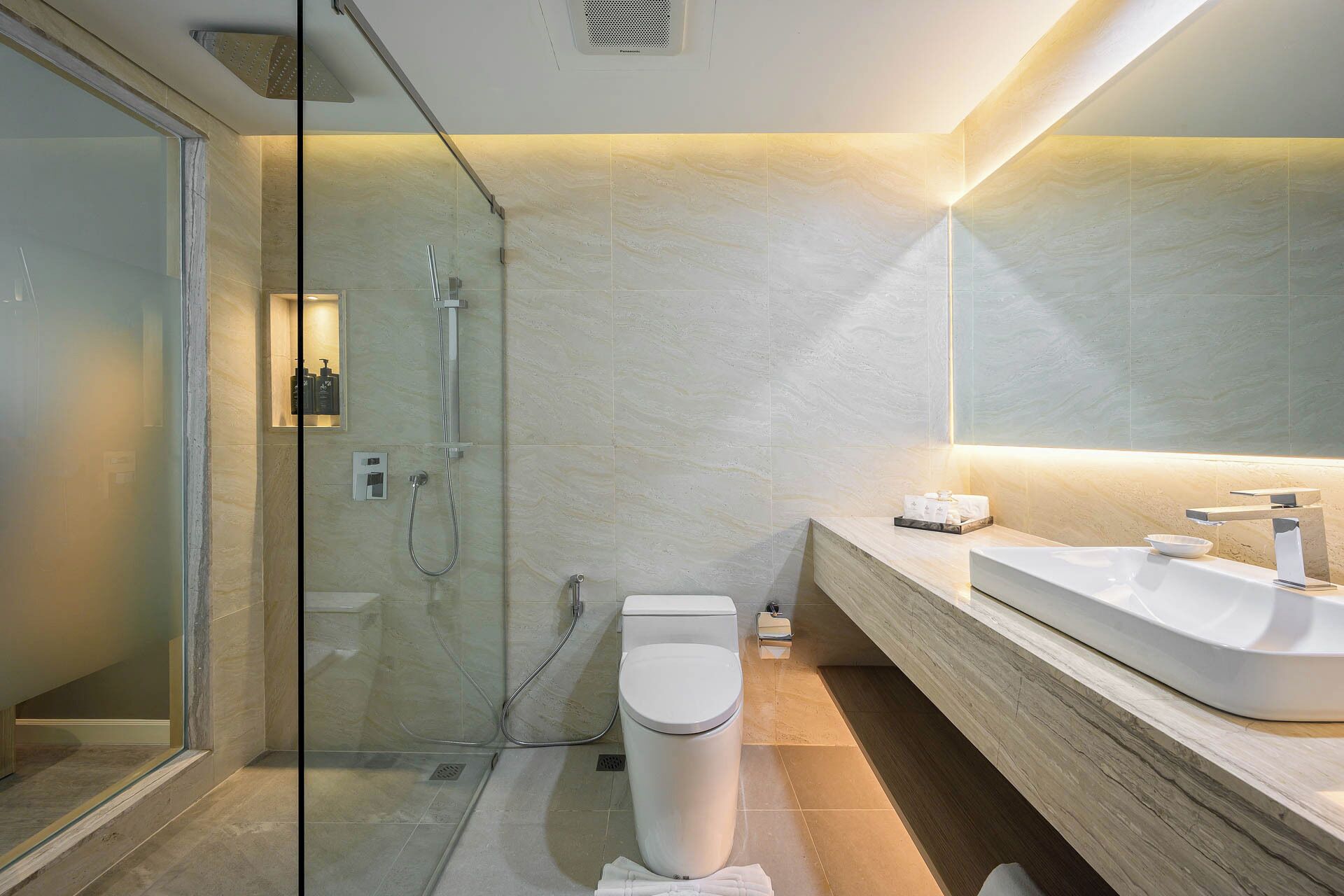 A modern bathroom with a glass-enclosed shower, a white toilet, and a wooden vanity with a large sink.
