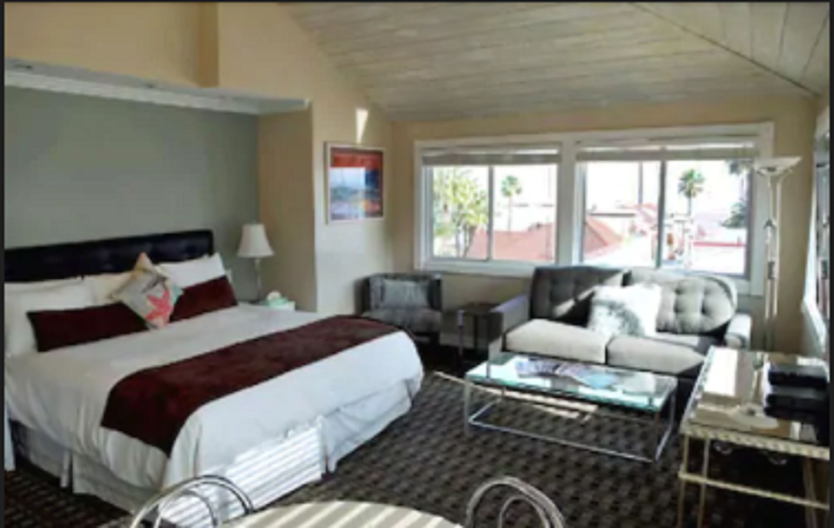 A hotel room with a large bed, a sofa, a coffee table, and a window with a view of palm trees.