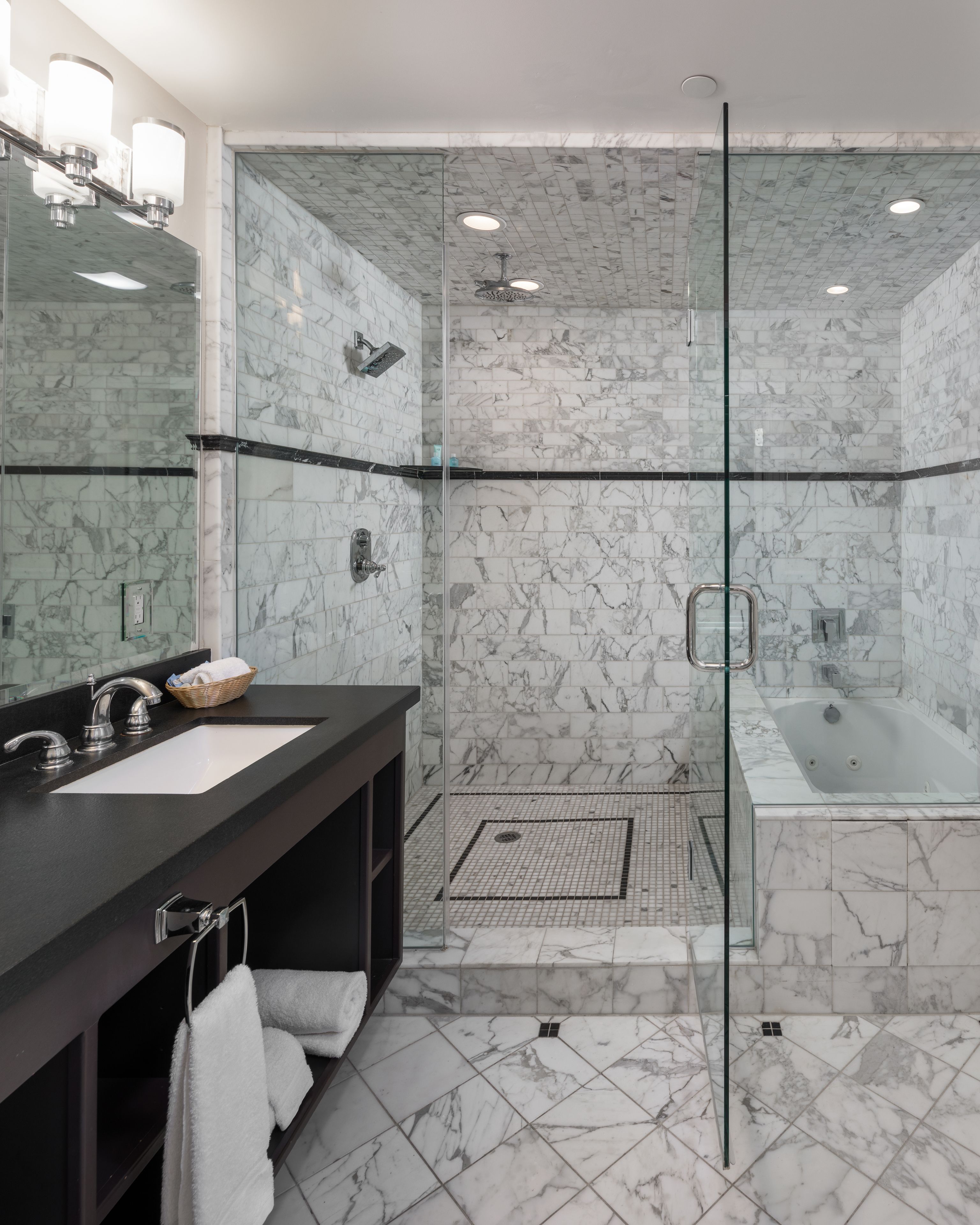 A modern bathroom with a glass-enclosed shower, a separate bathtub, and a vanity with a large mirror and dual sinks.