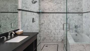 A modern bathroom with a glass-enclosed shower, a separate bathtub, and a vanity with a large mirror and dual sinks.