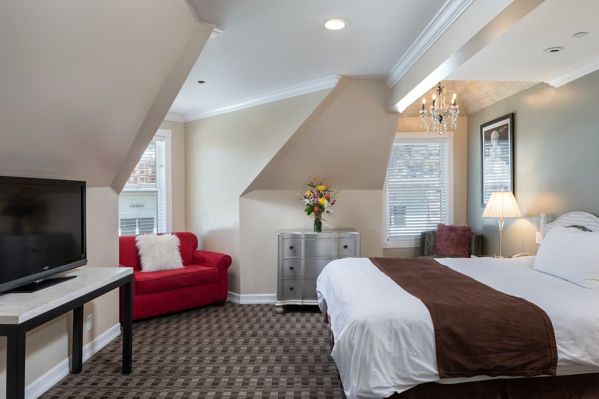Quarto de hotel com cama, sofá vermelho, televisão, penteadeira e candelabro.