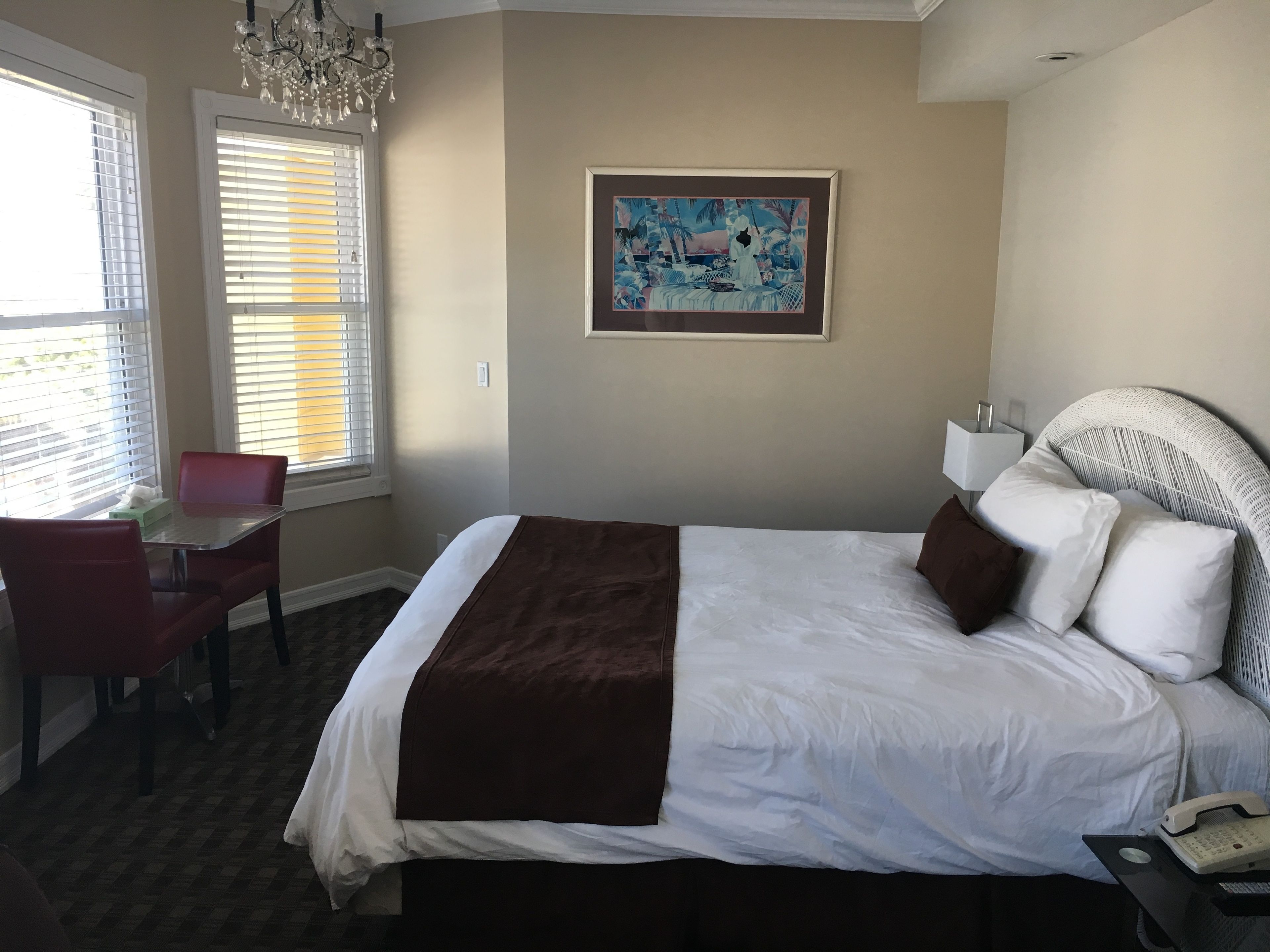 A hotel room with a large bed, a desk with a chair, a painting on the wall, and a chandelier.
