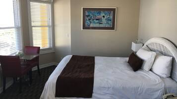 A hotel room with a large bed, a desk with a chair, a painting on the wall, and a chandelier.