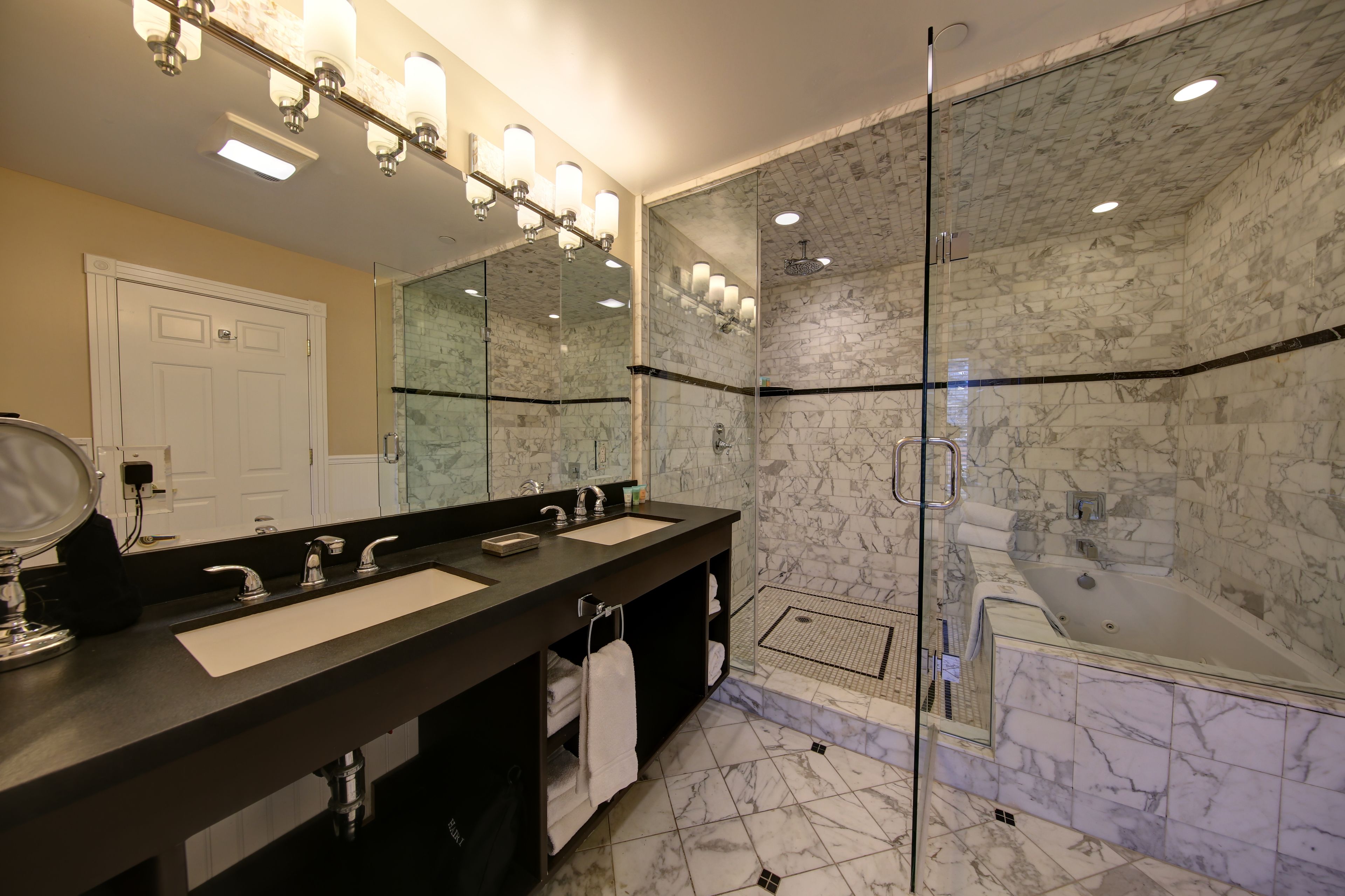 A modern bathroom with a large mirror, two sinks, a shower, and a bathtub.