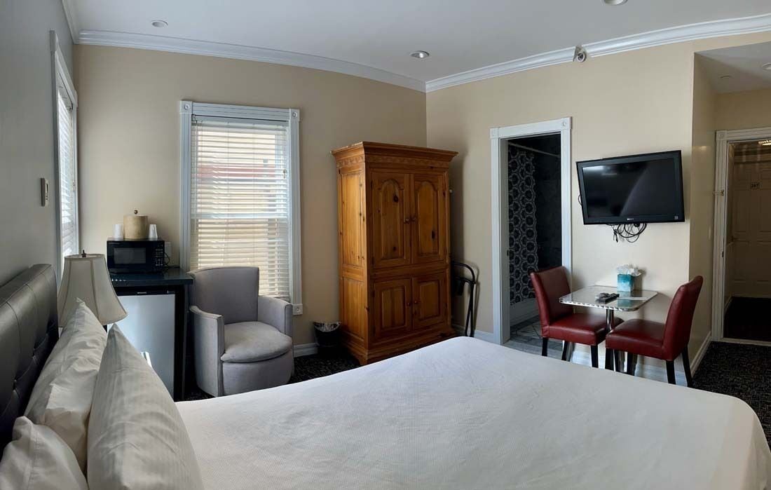 A hotel room with a bed, a desk with a microwave, a wardrobe, a TV, and two chairs.