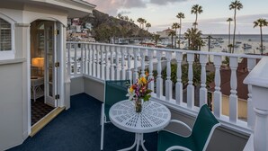 A balcony with a white railing, a round table with two chairs, and a vase of flowers. - Glenmore Plaza Hotel (Avalon)