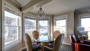 A dining area with a glass table surrounded by wicker chairs, large windows with blinds, and a chandelier. - Glenmore Plaza Hotel (Avalon)