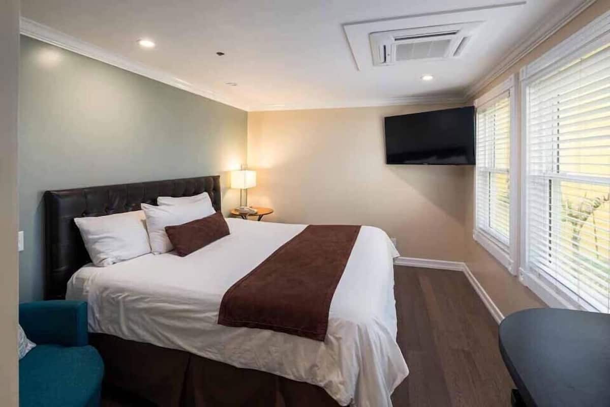 Quarto de hotel com cama, televisão presa à parede e janela com persianas.