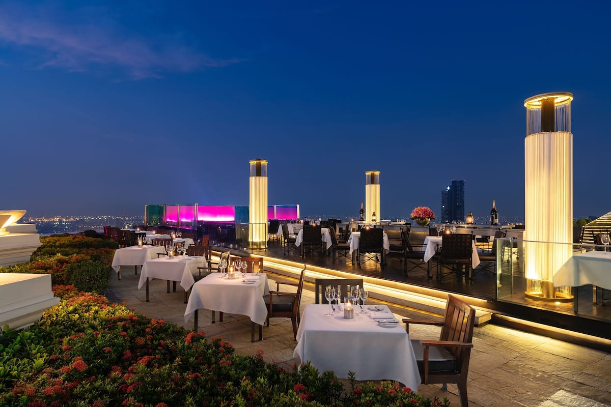 A rooftop restaurant with tables set for dining, overlooking a cityscape at dusk.