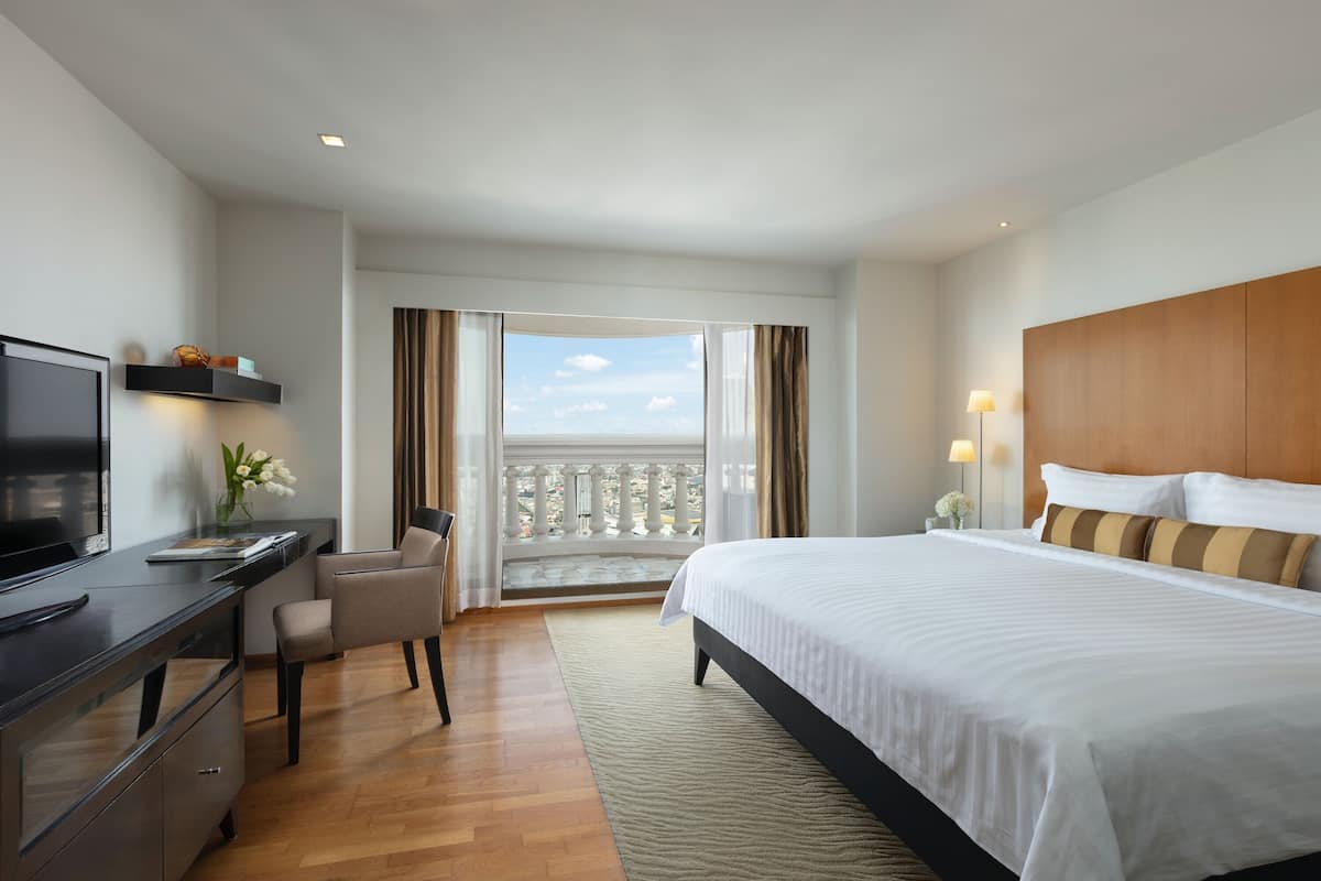 A hotel room with a bed, desk, TV, and a balcony with a view.