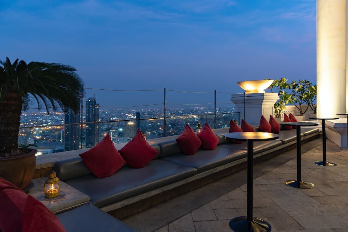 A rooftop terrace with seating and tables, overlooking a cityscape at dusk.