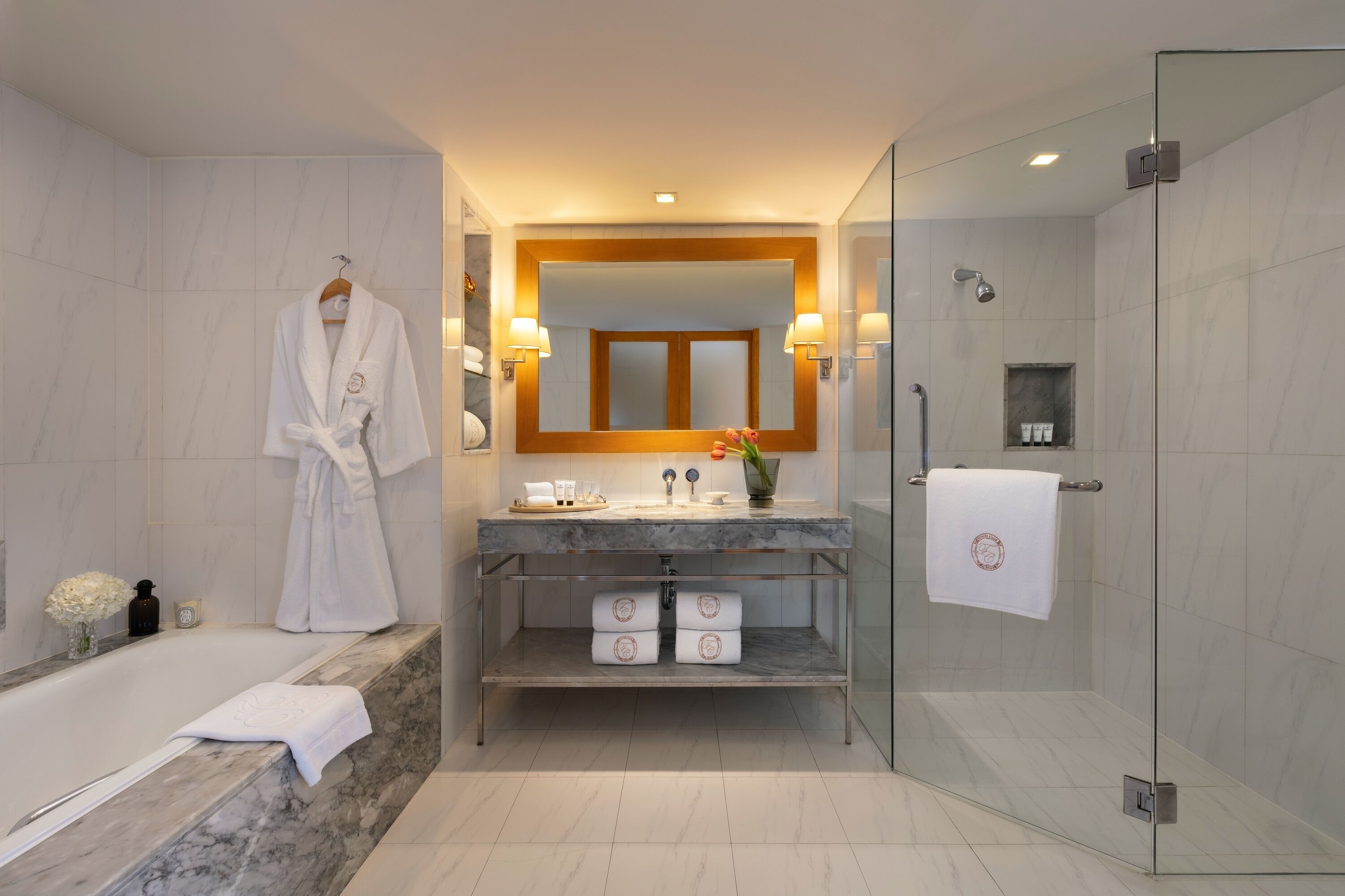 A modern bathroom with a glass-enclosed shower, a marble bathtub, and a vanity with a mirror and towel rack.