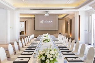 Un salón de conferencias con una larga mesa, sillas blancas y una pantalla de proyector mostrando 'lebuia hotels & resorts'.