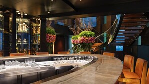 A modern bar area with a curved counter, multiple glasses, and a seating area with leather chairs.