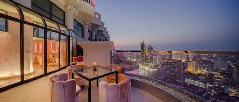 A high-rise hotel room with a glass table and chairs, a city view, and a balcony with a railing.