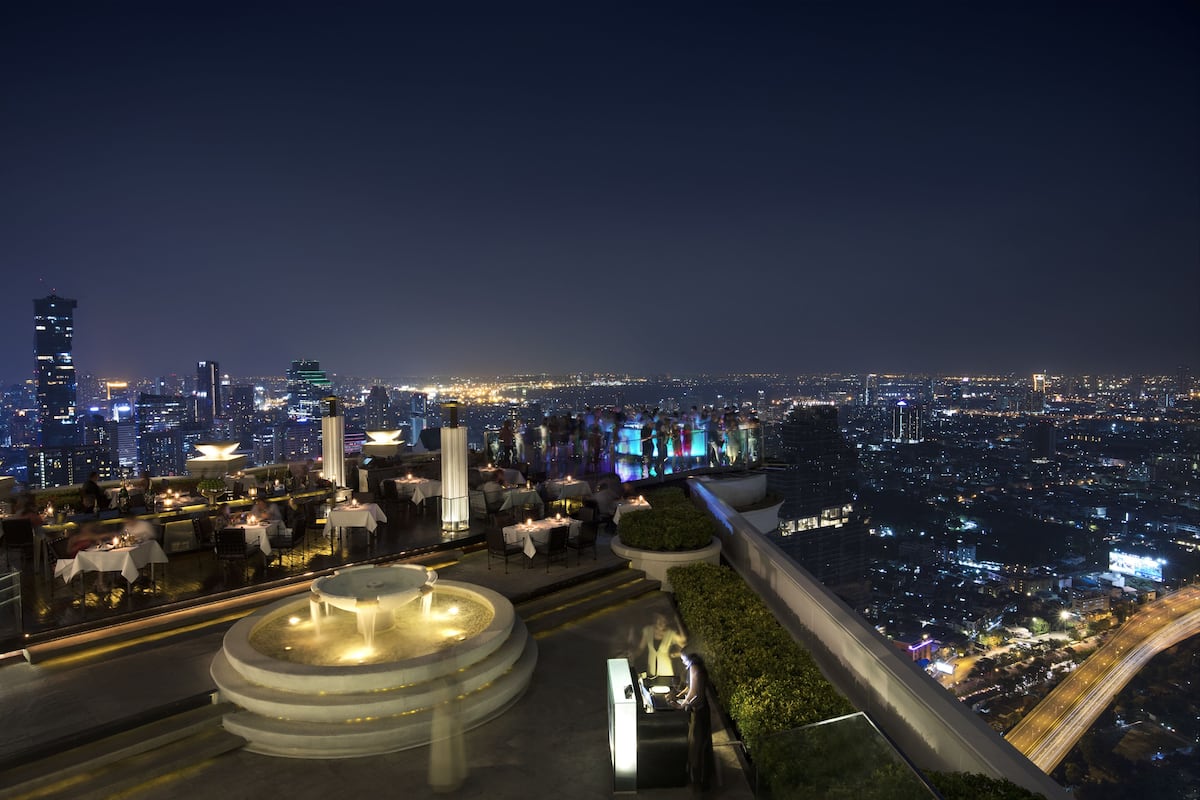 A rooftop restaurant with outdoor seating and a view of the city skyline at night.