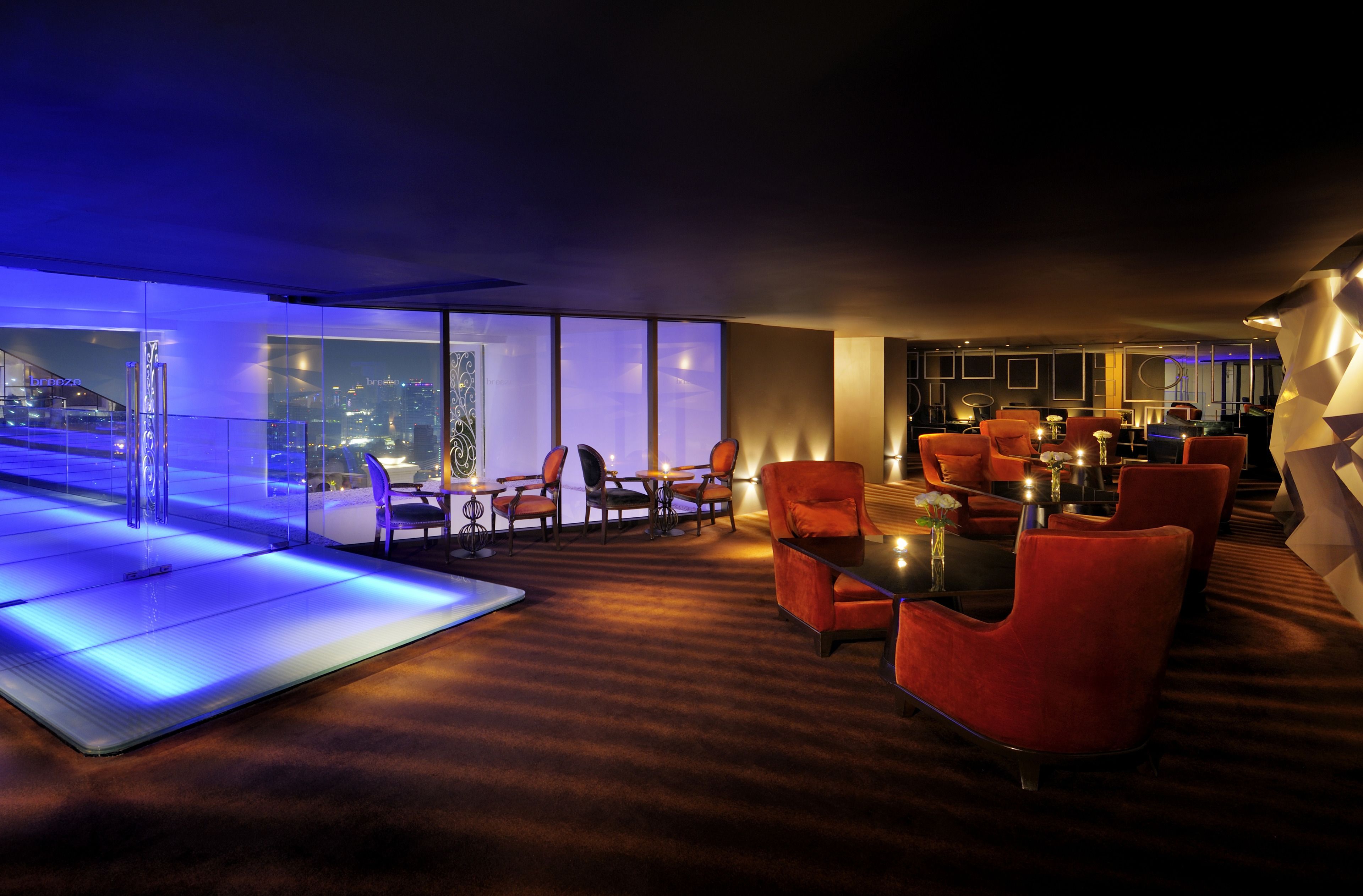 A modern lounge with red upholstered chairs, a glass partition, and a city view.