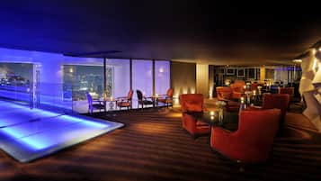 A modern lounge with red upholstered chairs, a glass partition, and a city view.