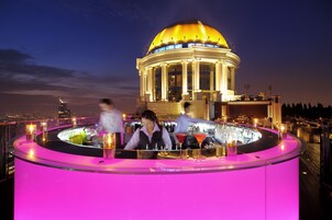 Un bar con tonalidades rosadas, una gran estructura en forma de cúpula dorada al fondo y un paisaje urbano al anochecer.