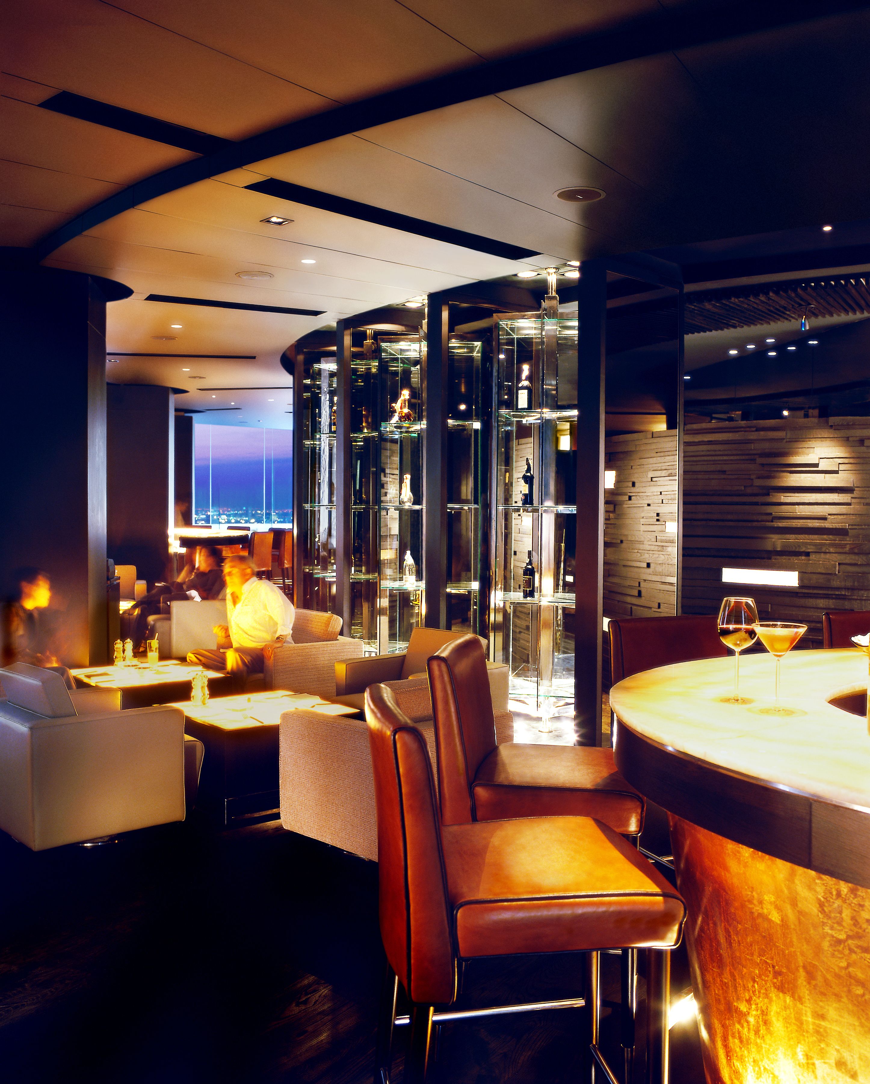 Un restaurant moderne avec un intérieur élégant, des cloisons en verre, des sièges en cuir et un espace bar.