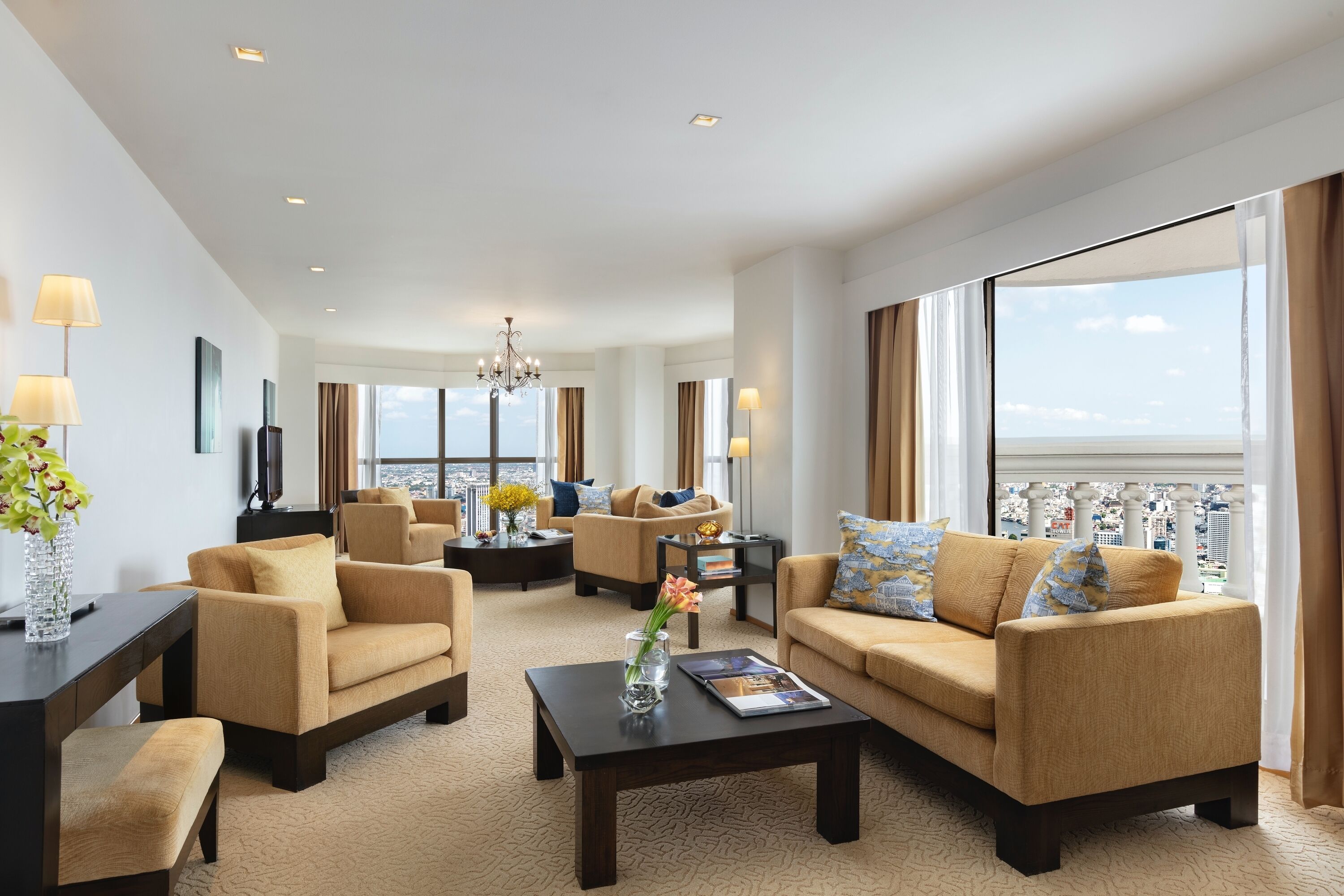 A spacious living room with beige sofas, a coffee table, and a TV. Large windows offer a view of the city and the sea.