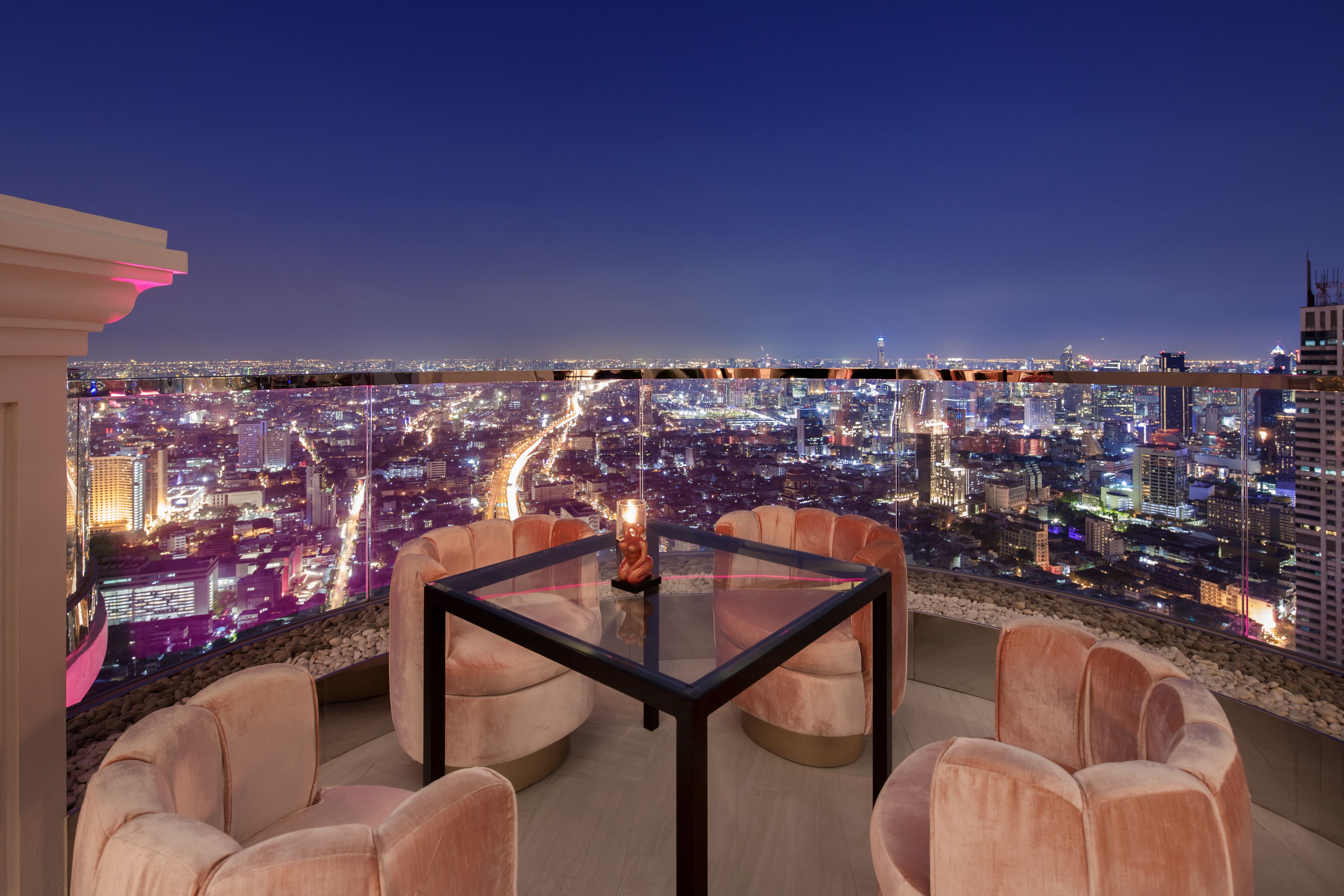 A high-rise room with a city view, a glass table, and plush seating.
