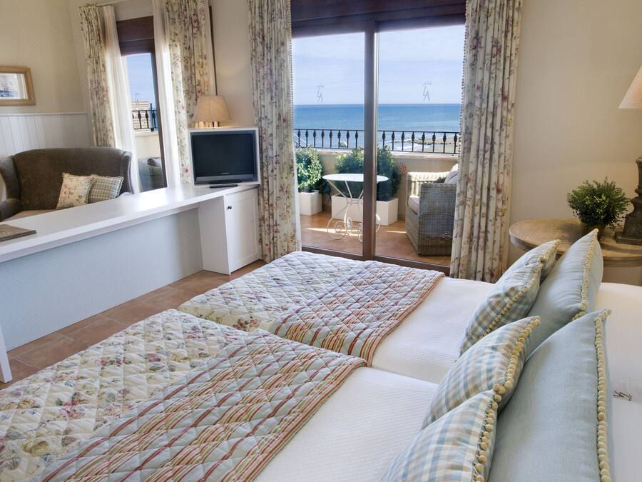 A bedroom with a bed, a desk, a TV, and a view of the sea.