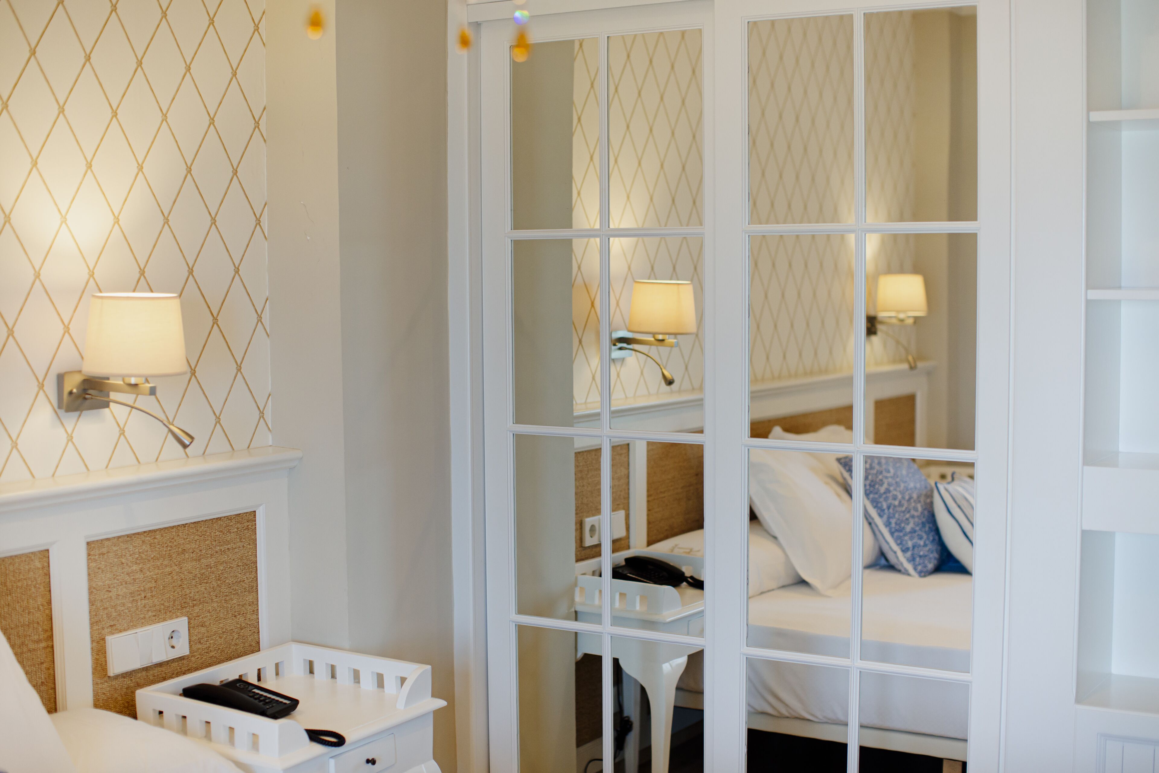Una habitación de hotel con cama, lámparas de noche, teléfono y una pequeña mesa blanca.