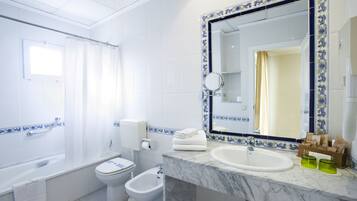 A bathroom with a bathtub, toilet, bidet, and a sink with a mirror.
