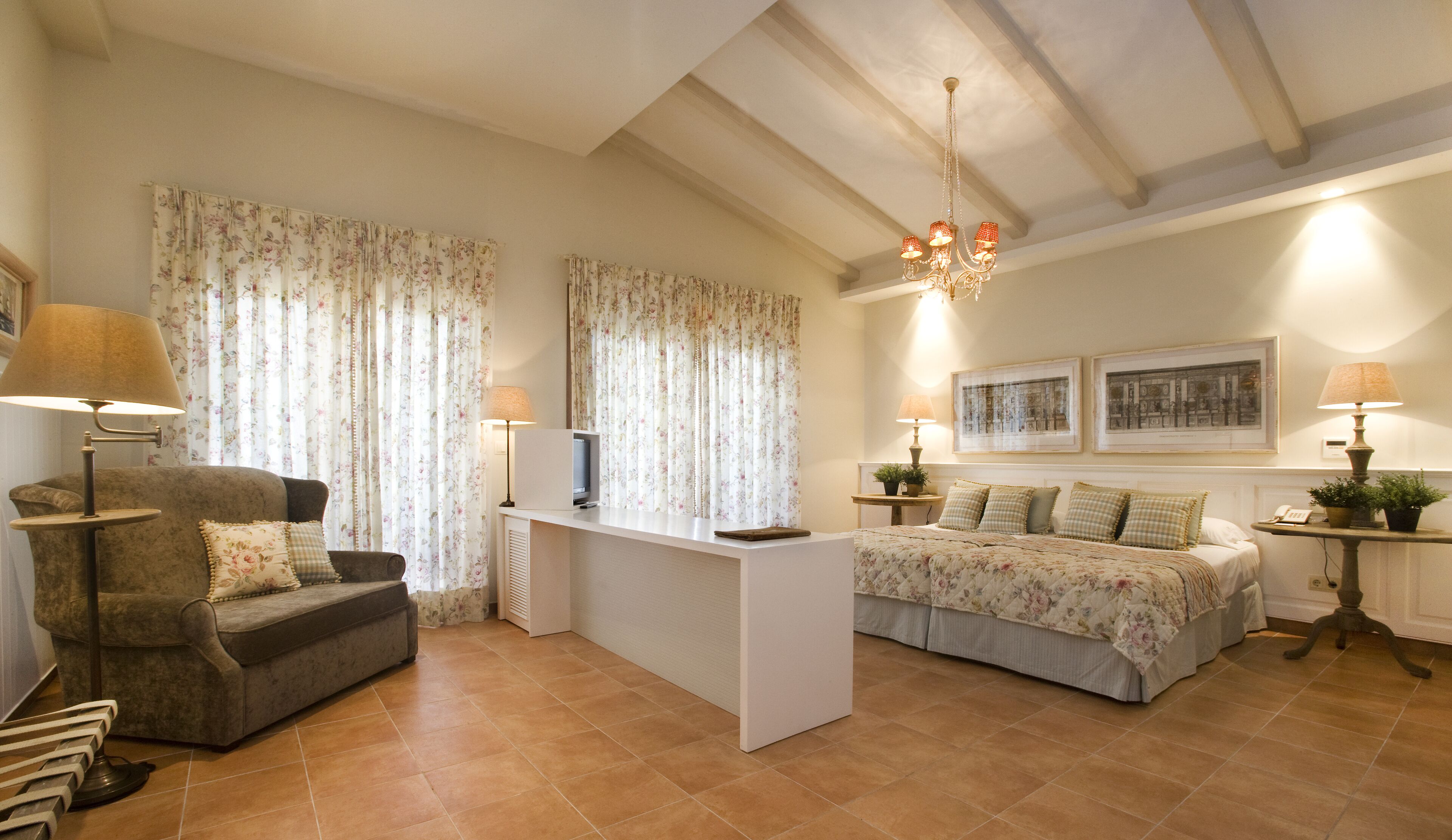 A cozy living room with a sofa, a coffee table, a TV, and a bed with floral bedding.