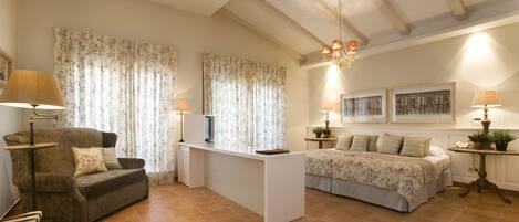 A cozy living room with a sofa, a coffee table, a TV, and a bed with floral bedding.