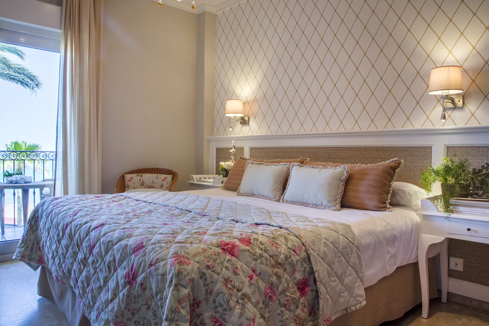 Habitació d'hotel amb un llit gran, dues taules de nit, una estant i una finestra amb cortines que donen vistes a palmeres.