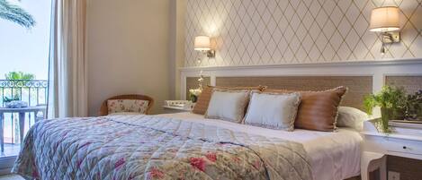 A hotel room with a large bed, two bedside tables, a nightstand, a window with curtains, and a view of palm trees.