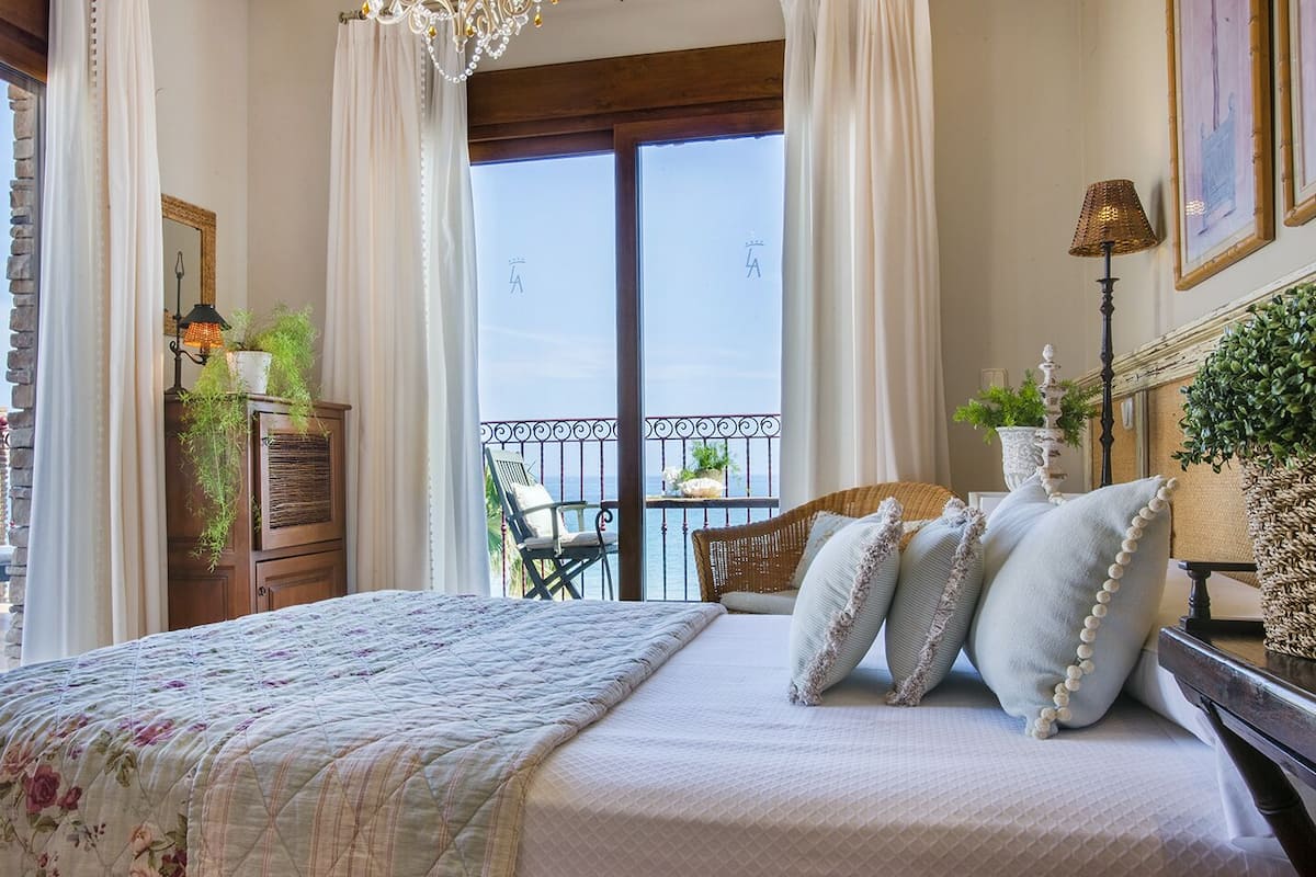 Un dormitorio con una cama grande, un balcón con una silla y vista al mar.