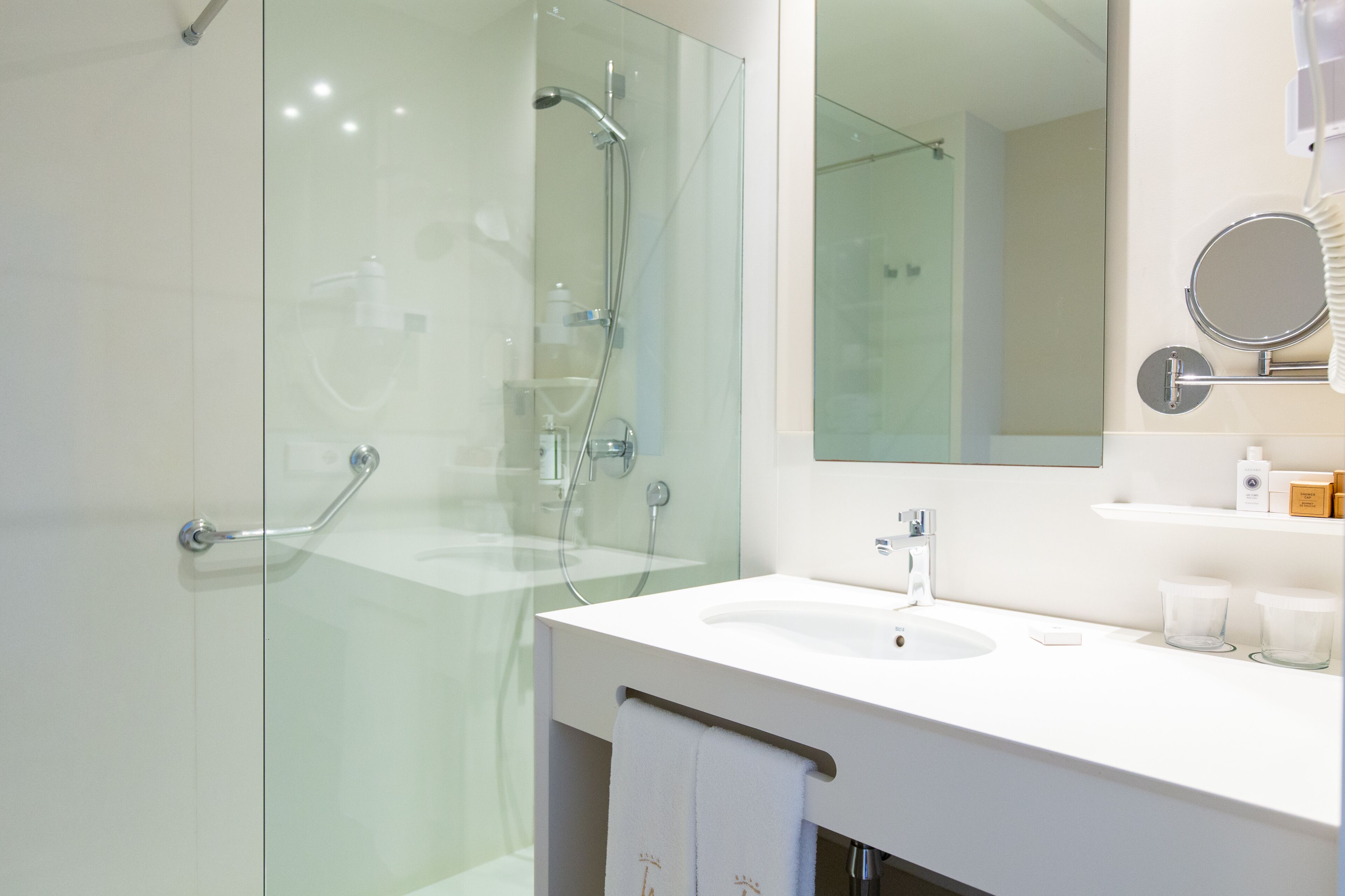 A modern bathroom with a glass shower enclosure, a white sink, and a mirror with a round frame.