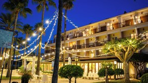 A hotel with multiple balconies, string lights, palm trees, and outdoor seating. - Hotel Los Ángeles (Denia)